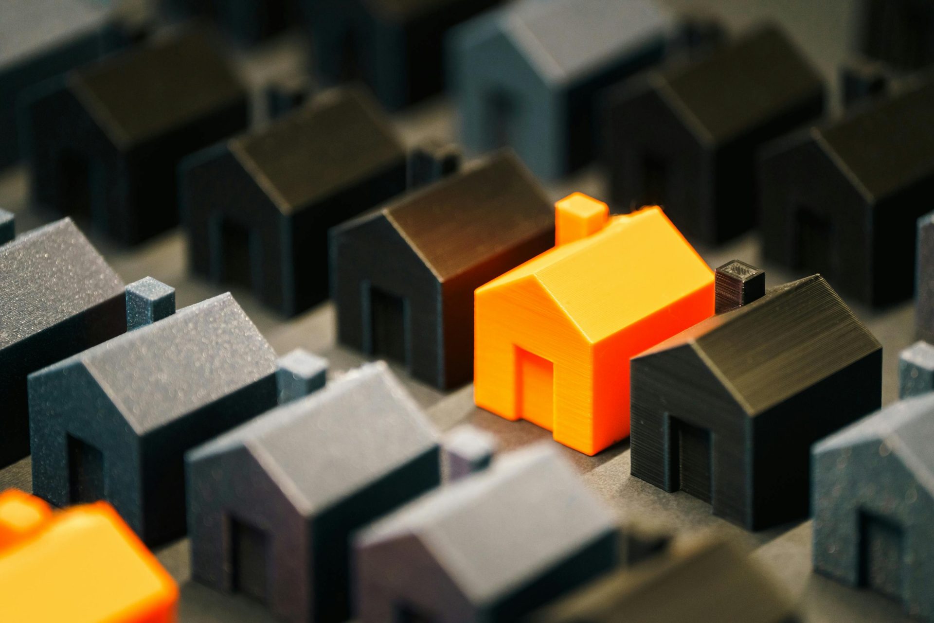 Striking orange model house stands out among black miniature houses, symbolizing real estate choices.